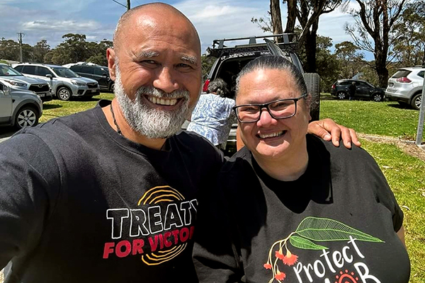 Outreach Lake Tyers Two people smiling and posing for the camera. They are wearing a 'Treaty for Victoria' shirt and another shirt with a gum tree design.